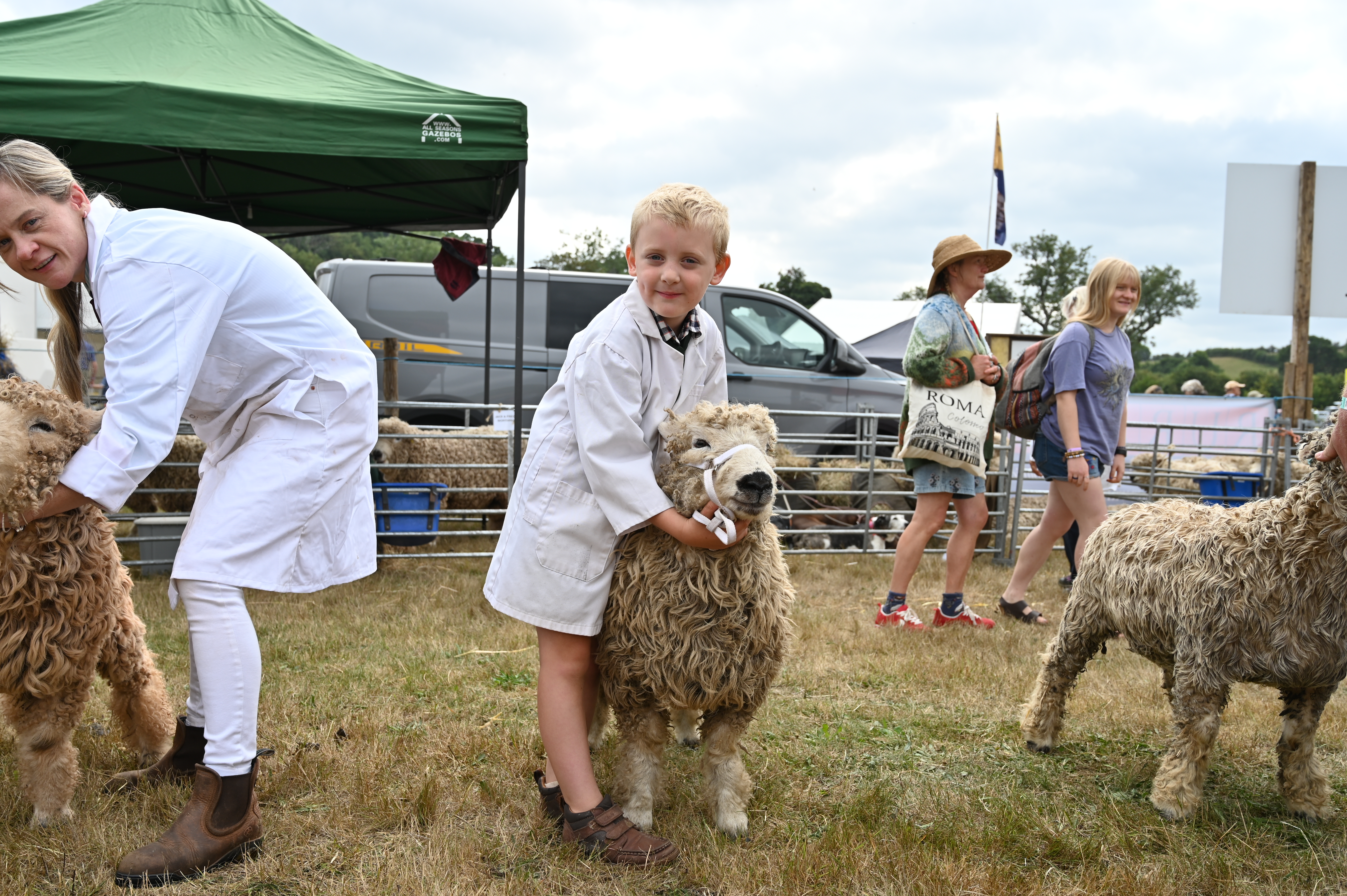 Young boy stands in a white coat with his sheep