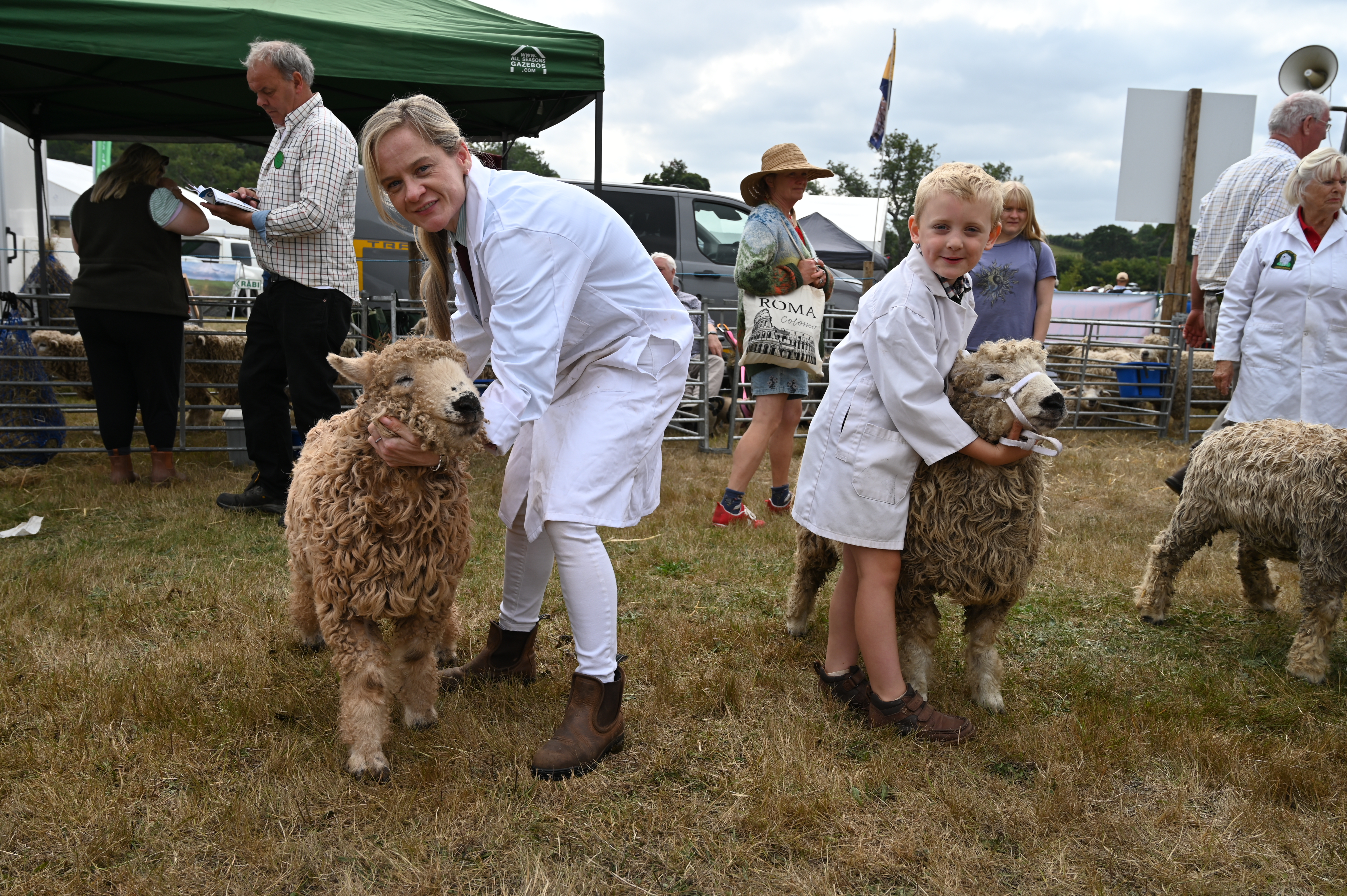 Boy and lady in white coats stand with their sheep at a show
