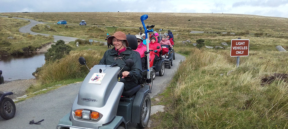 Group of people using mobility scooters on a military ring road on the moor
