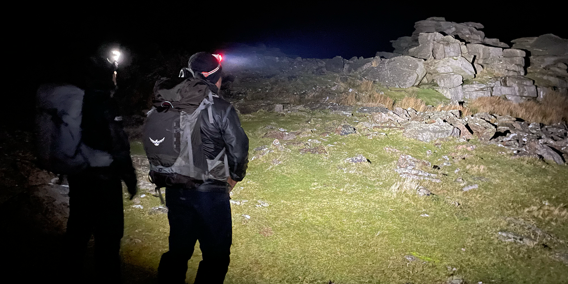 Two rangers with head torches shining light onto a Tor