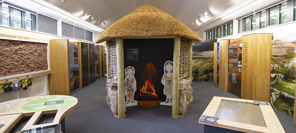 Model bronze age roundhouse with cardboard cut-out cartoon characters inside