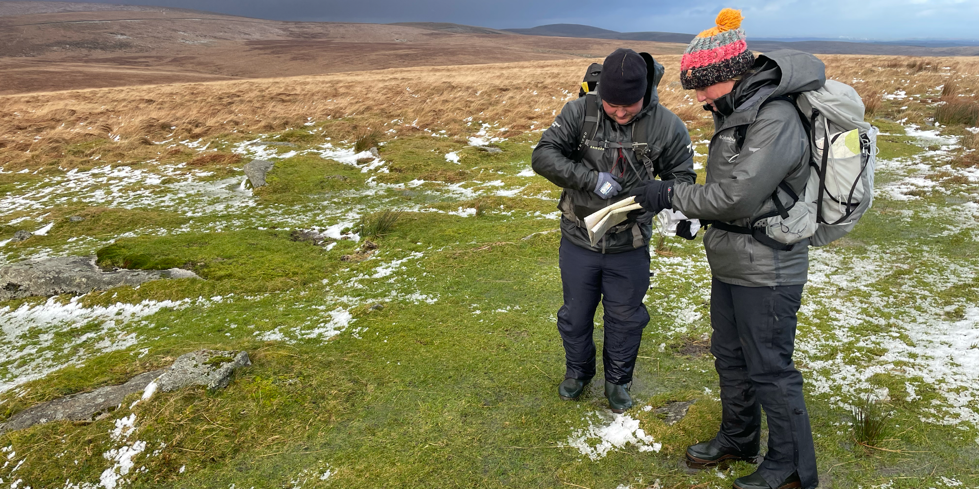 Two rangers on a snowy moor reading a map