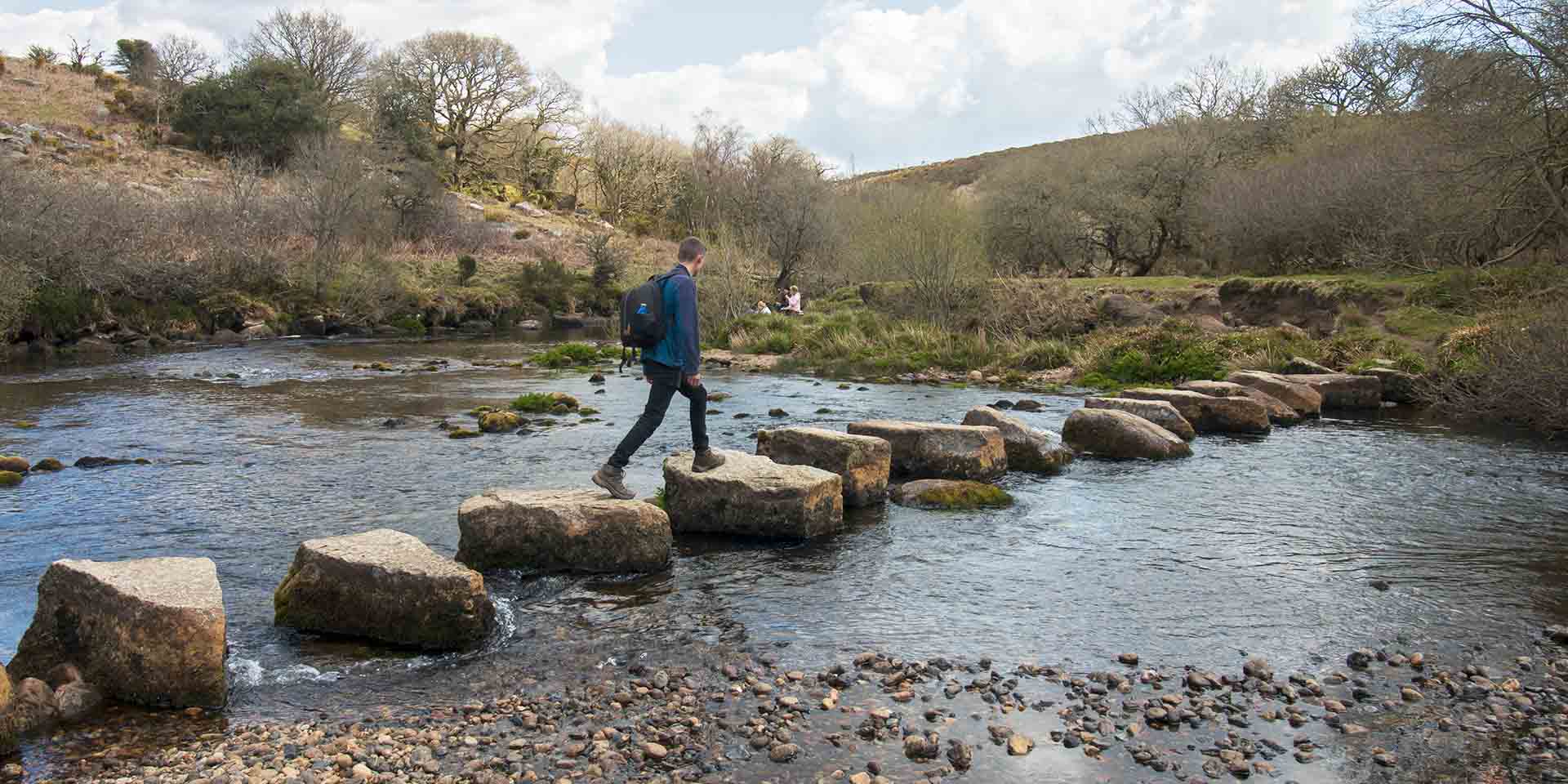 Person crossing large stepping stones over shallow river