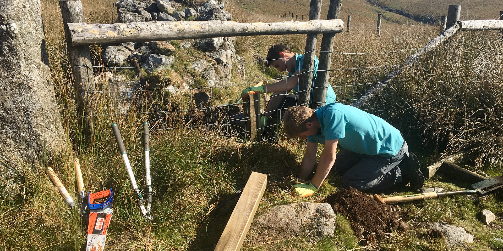 Two people work on repairing a fenced area. 