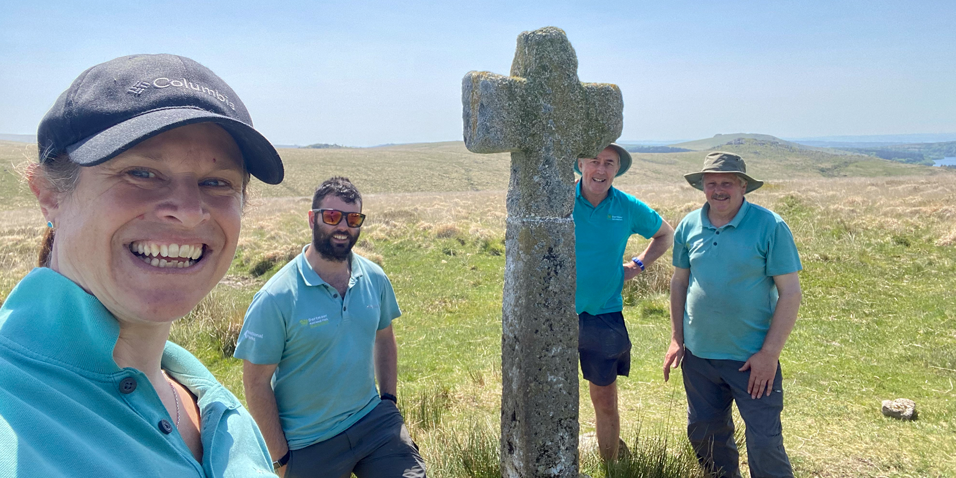 Four rangers stand around a stone cross they have recently repaired
