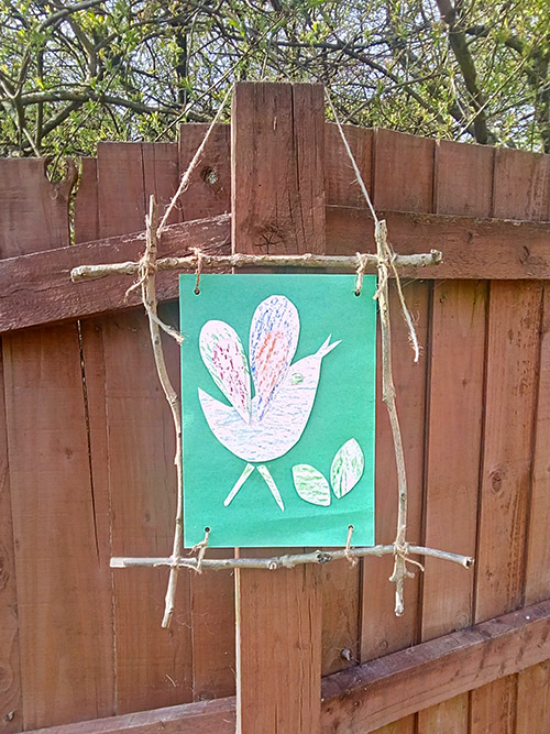 Bark rubbing picture in twig frame hung from a garden fence