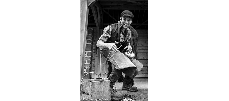 Farrier Nick working on a horse's hoof and smiling