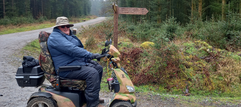 Man sat on tramper on the Bellever Train beneath the finger post sign showing the way. 