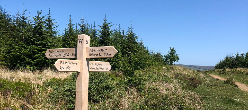 New finger post sign showing the way on the Bellever Miles Without Styles route. Sign sits beneath a bright clear sky. 