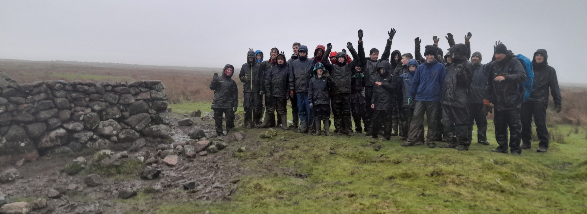 Group of young adults stand by a tor celebrating in the rain
