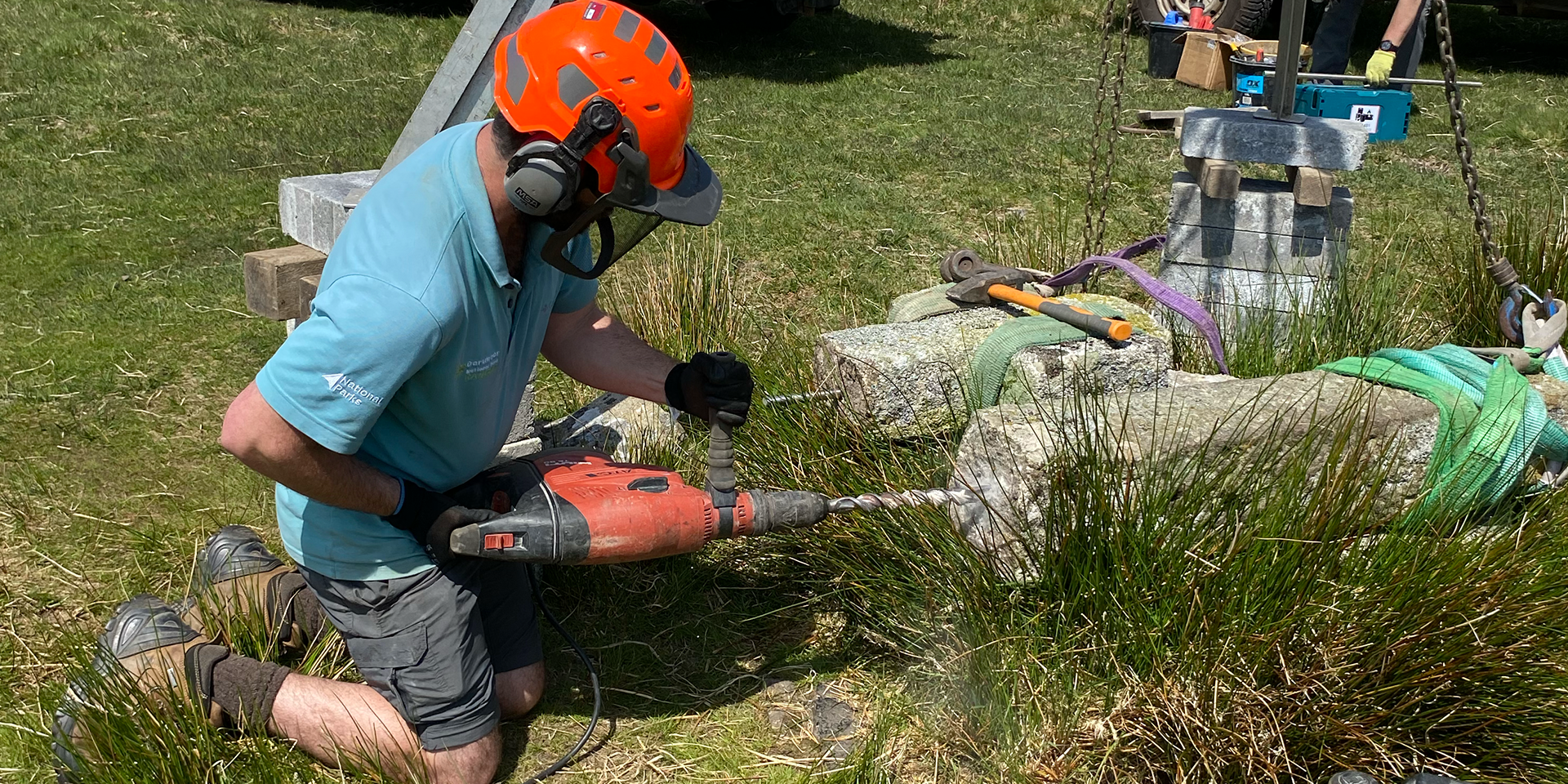 Ranger holding drill working to repair a stone cross in summer
