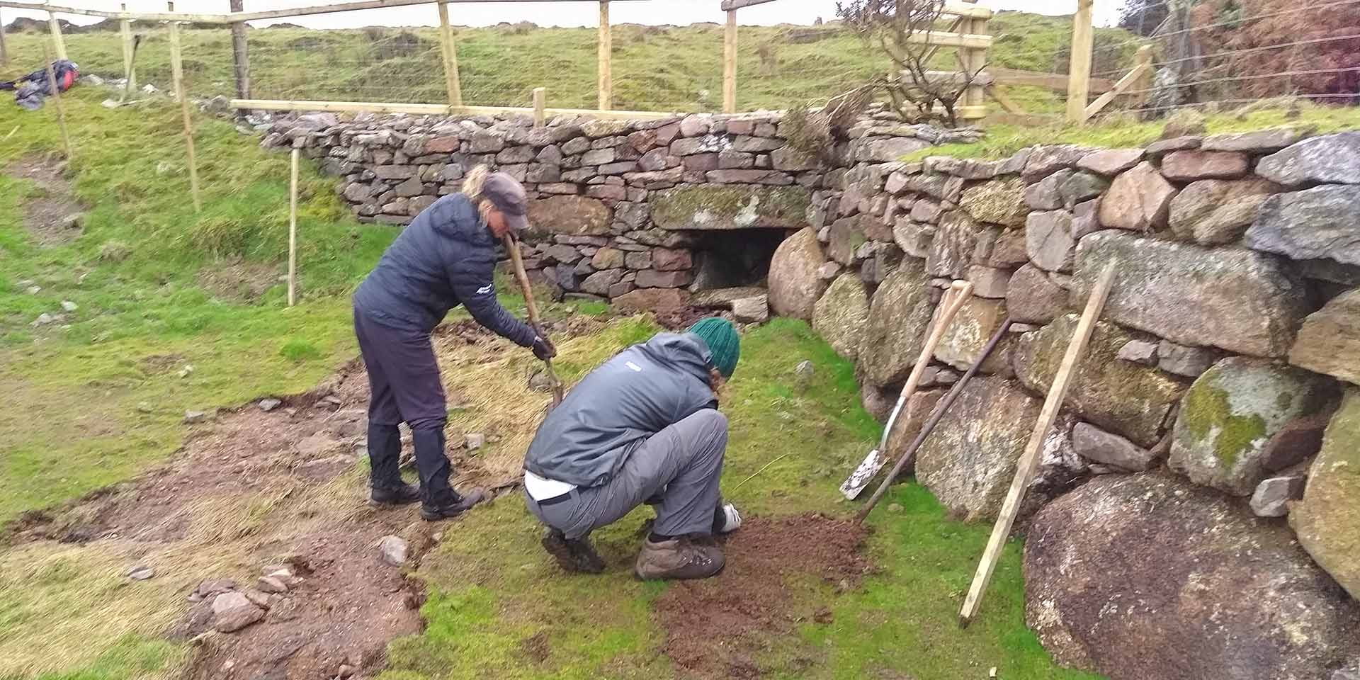 Two people repairing a stone wall