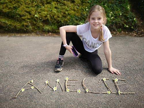 Girl smiling next to sticks and daisies spelling 'Amelie